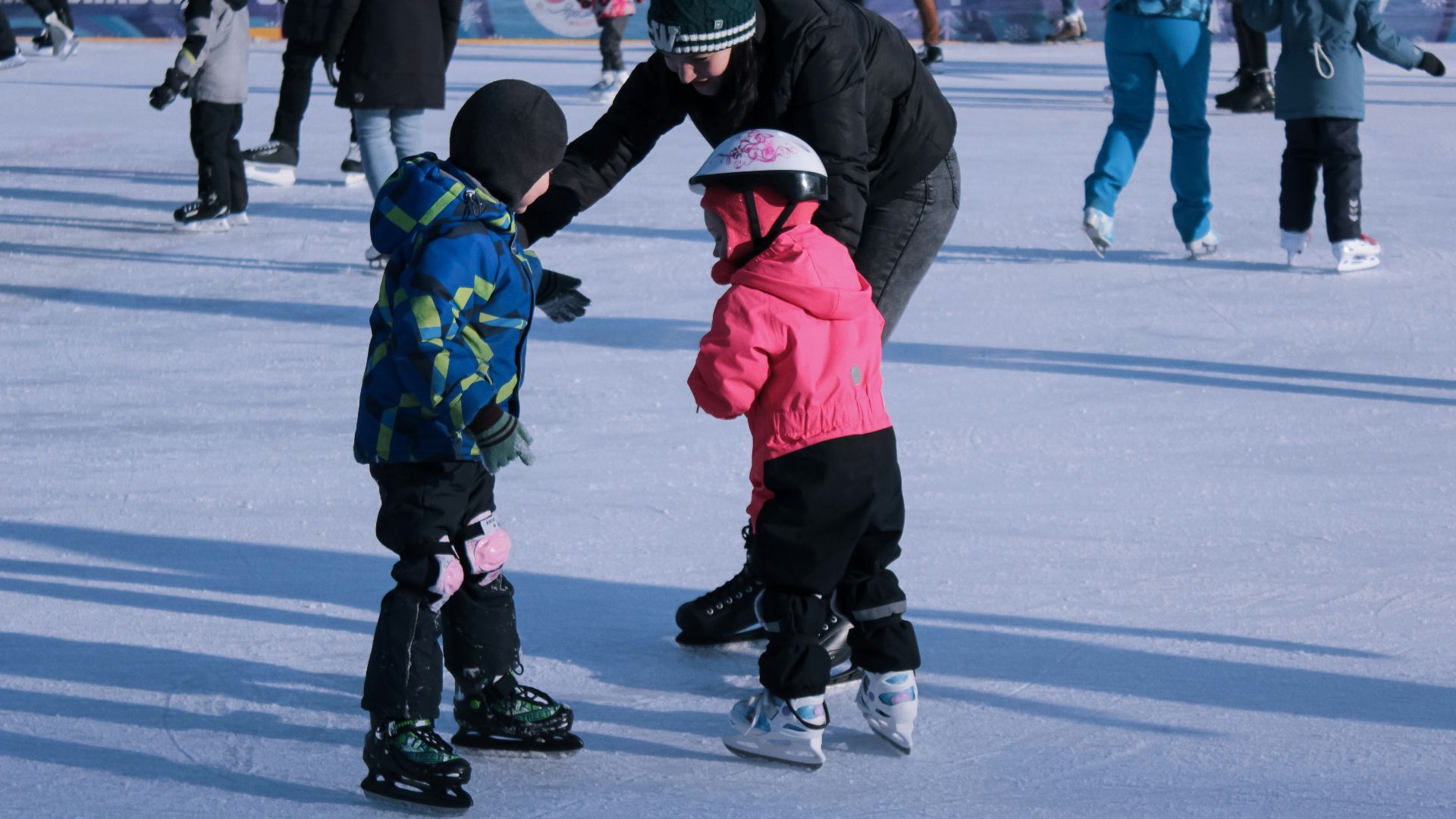 2 children in red jacket and black pants playing ice hockey