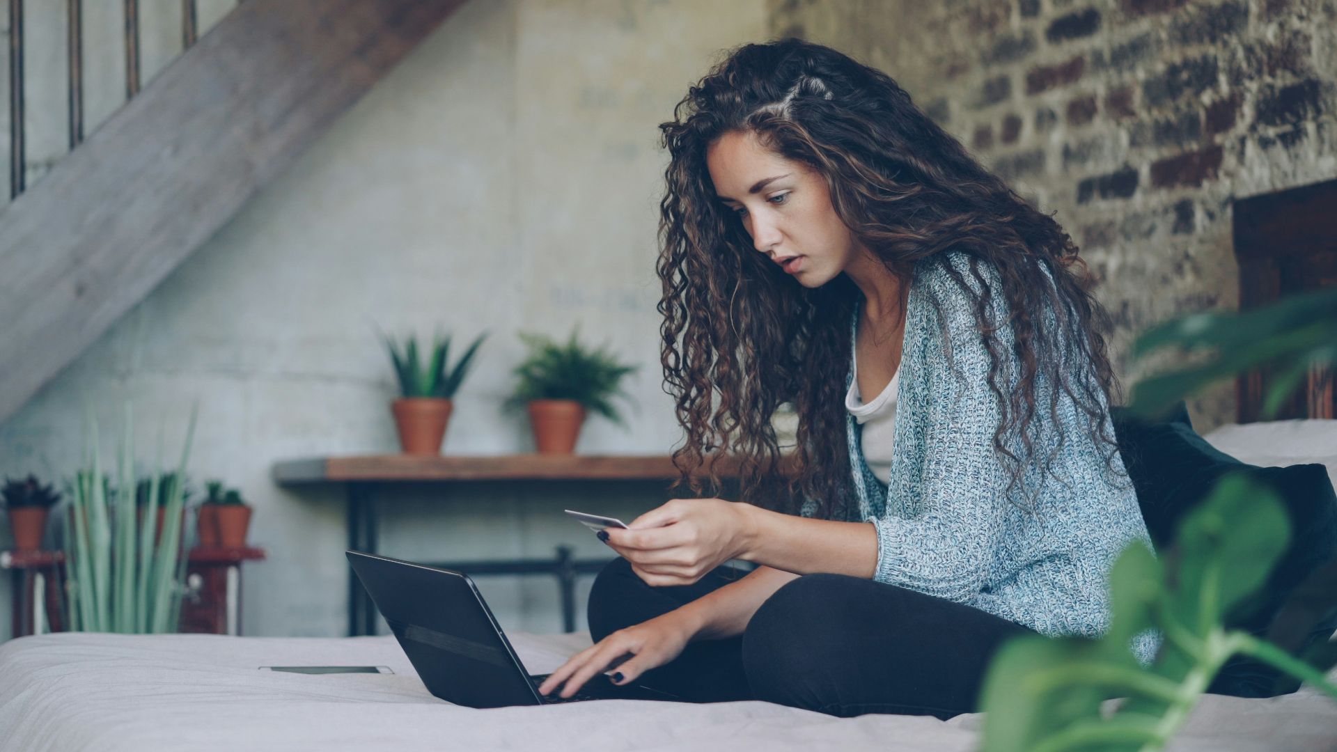 Woman using laptop and credit card on bed.