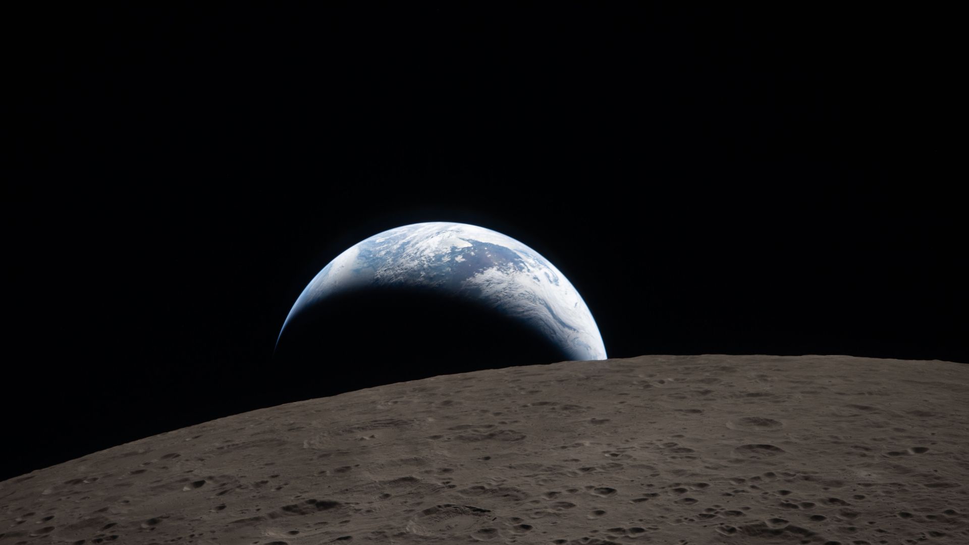 art002e009288 (April 6, 2026) – Earthset captured through the Orion spacecraft window at 6:41 p.m. EDT, April 6, 2026, during the Artemis II crew's flyby of the Moon. A muted blue Earth with bright white clouds sets behind the cratered lunar surface. The 