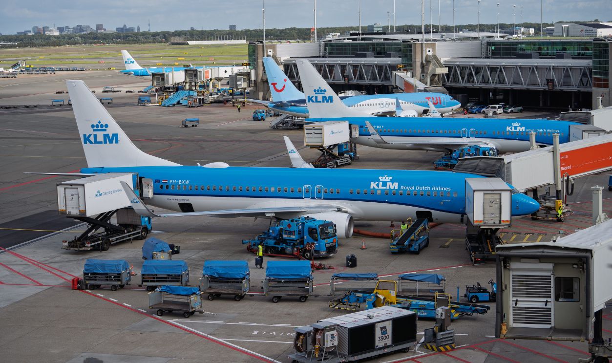 Multiple KLM aircraft at Amsterdam Schiphol Airport terminal with blue ground support equipment