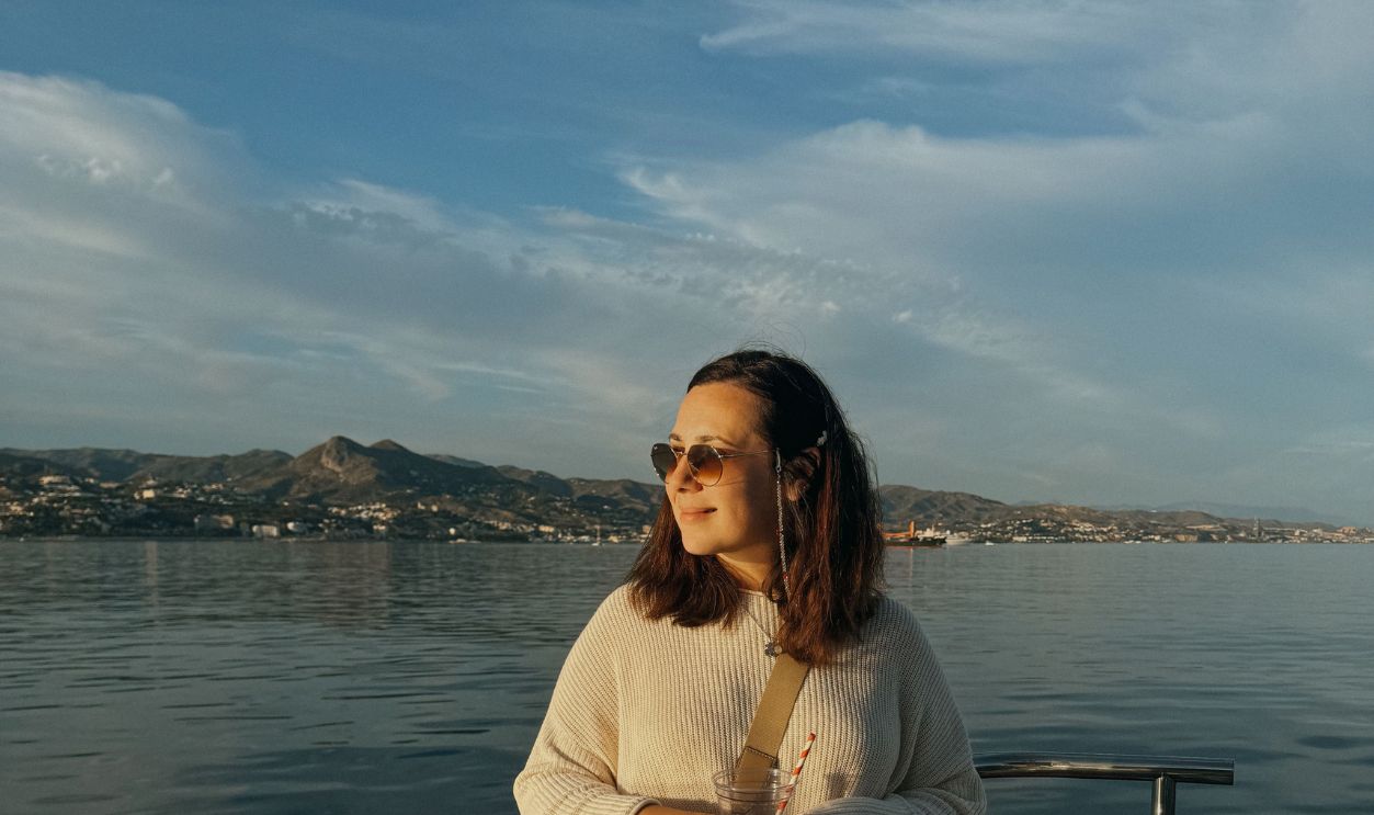 A woman stands on a boat, enjoying a sunny day at sea, wearing sunglasses 
