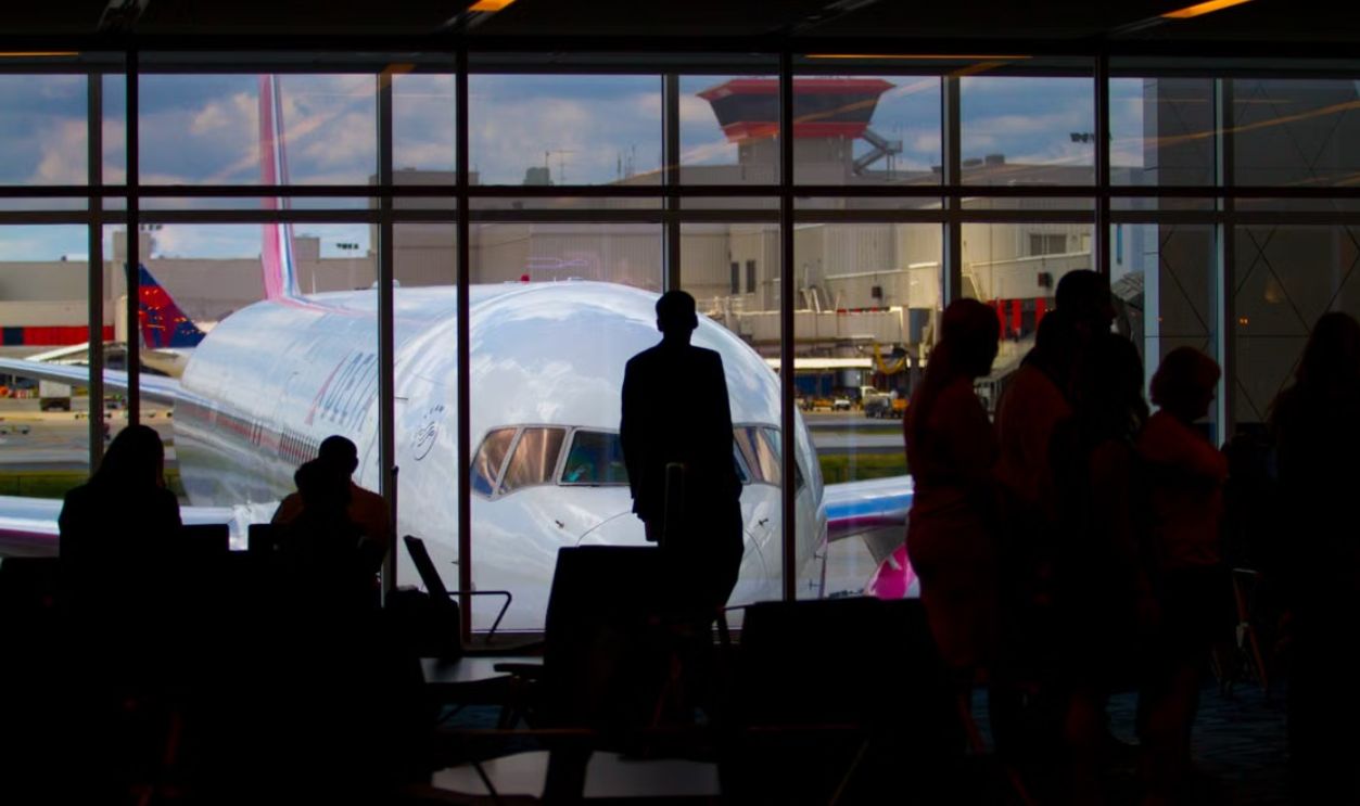 Silhouettes of travelers waiting at an airport terminal with an airplane visible through the window