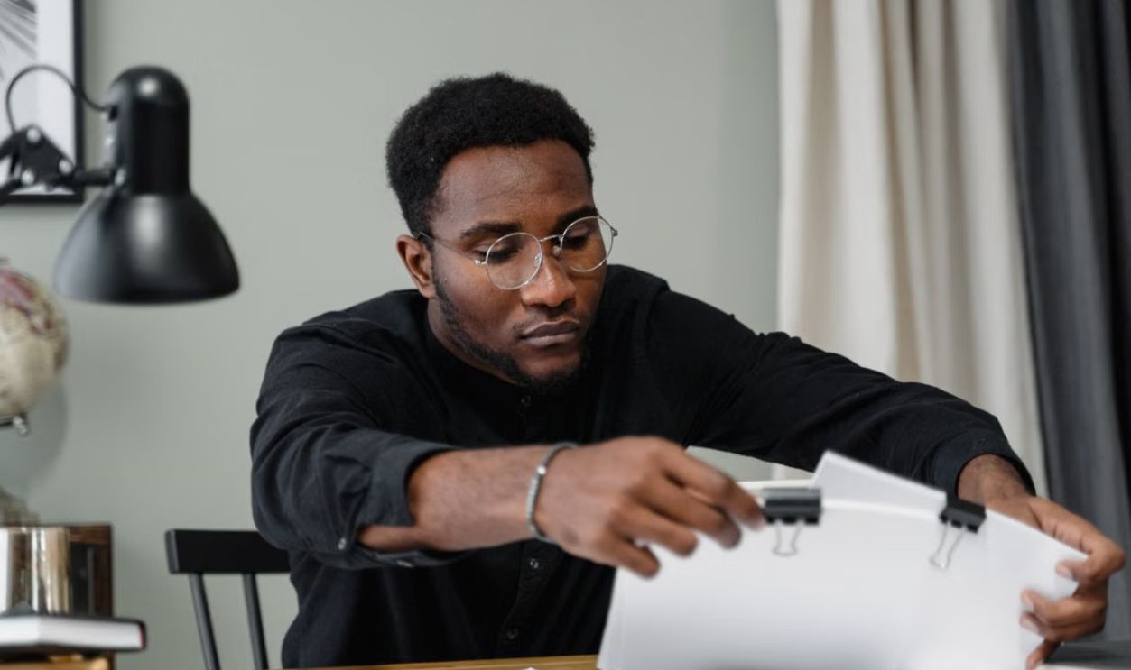 Professional man with glasses reviews documents at a desk in an office setting, emphasizing concentration