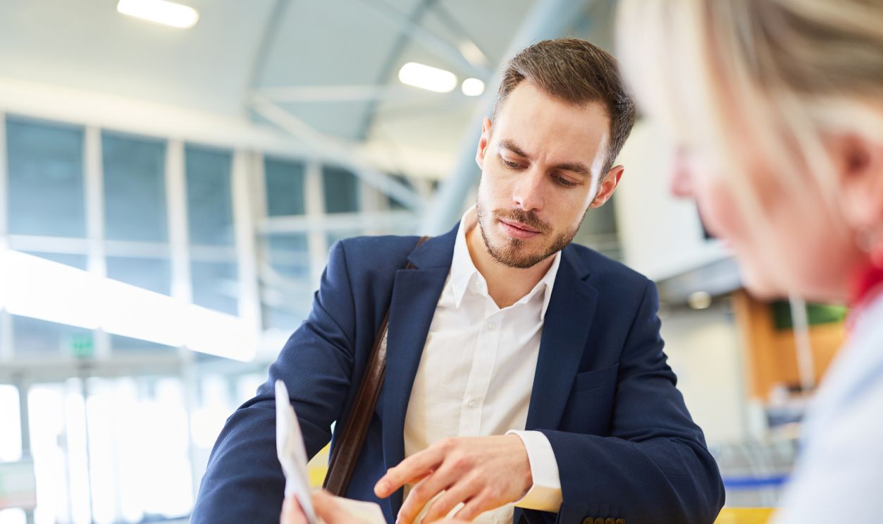 Service agent at the check in counter controls boarding pass or pass from a business man