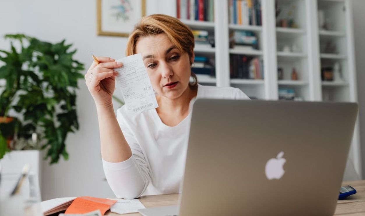 Woman concentrating on receipts while using a laptop, reflecting financial stress.
