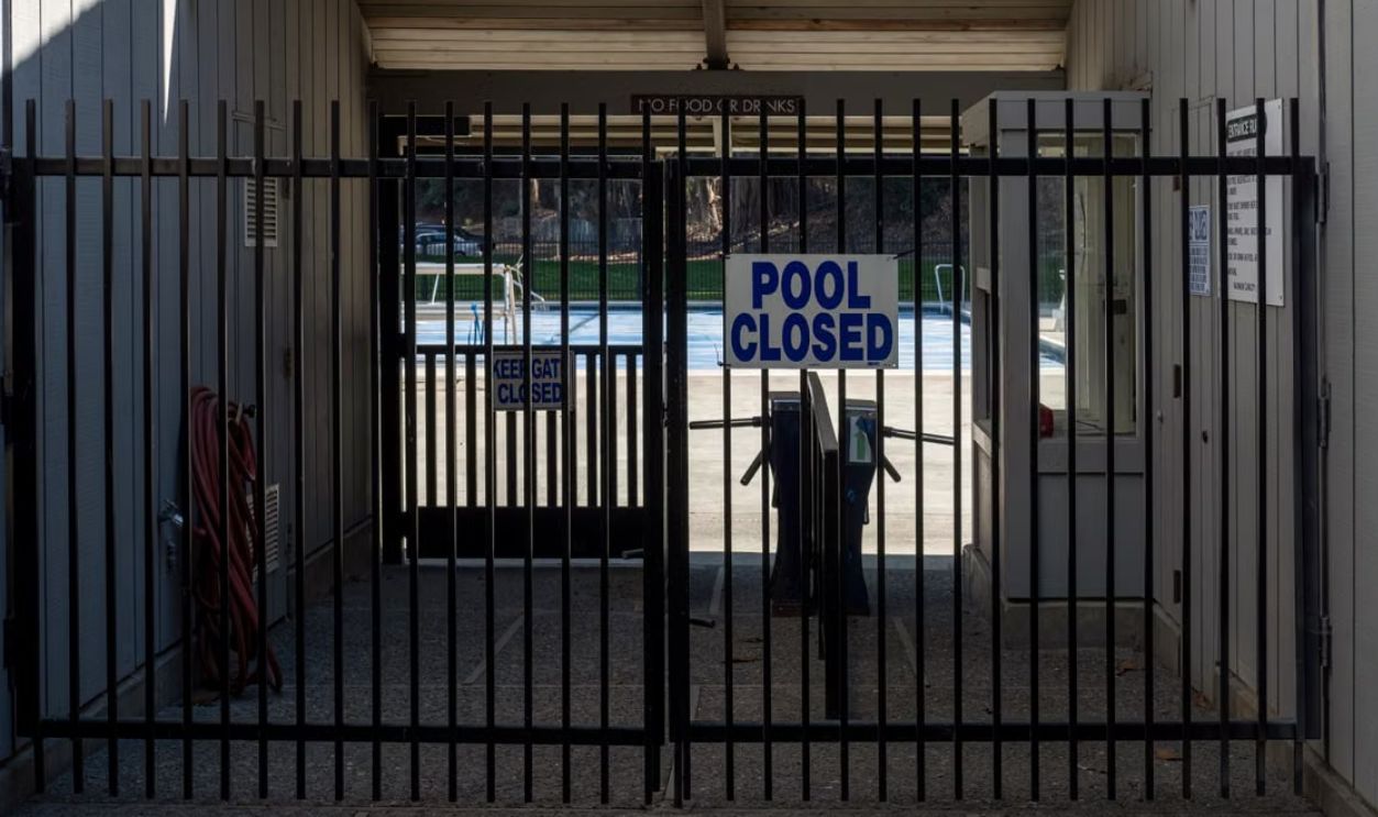 Iron gate blocking a closed community pool entrance with a clear sign.