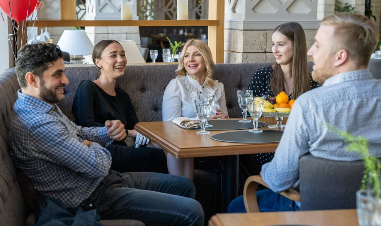 Five adults having a joyful conversation in a cozy restaurant setting indoors.