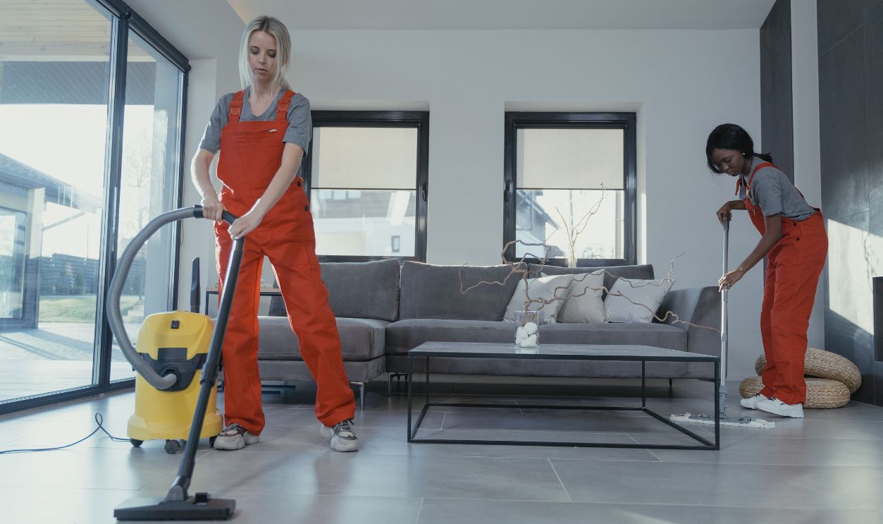 Two women in red overalls vacuuming and sweeping