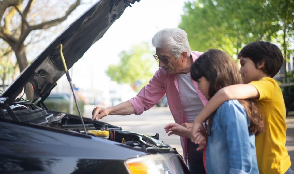 Grandfather shows his grandchildren car engine mechanics outdoors, teaching them about car maintenance