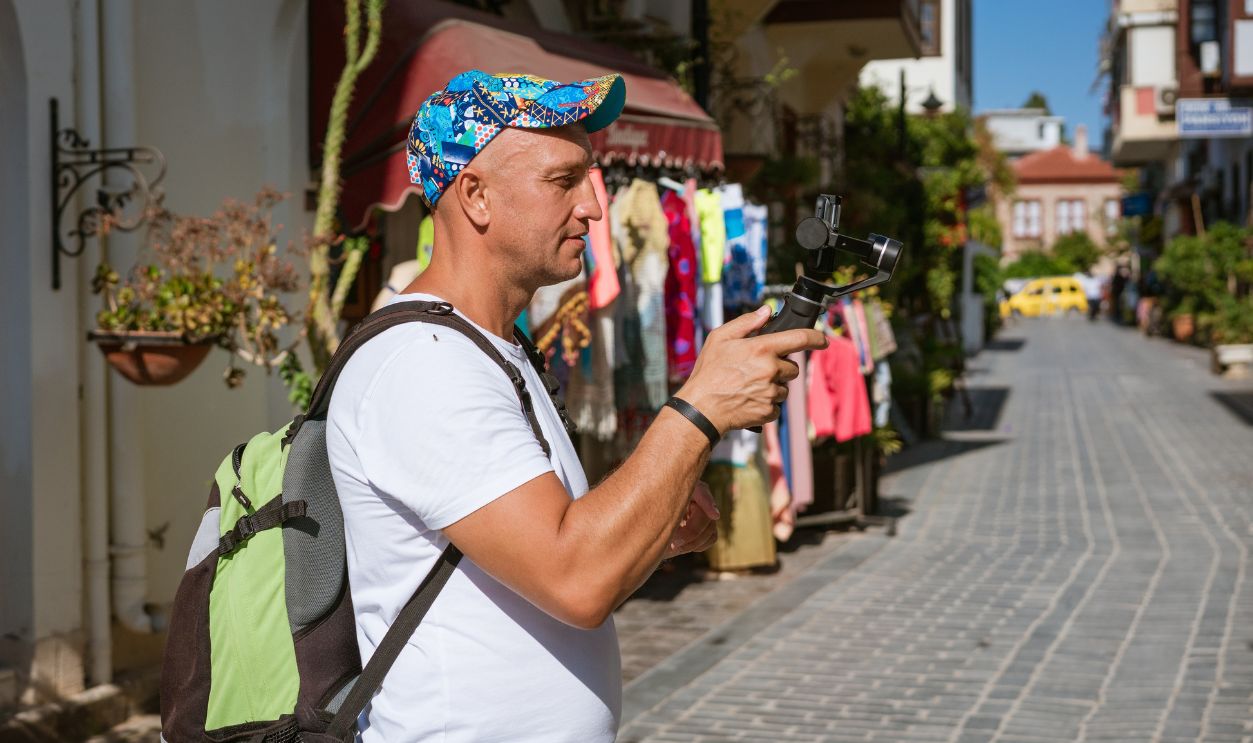 Caucasian vlogger films with gimbal at shopping street with clothing boutiques. Suitable for content creator brand, vlogger gear, travel blog, tourism magazine and lifestyle guide.