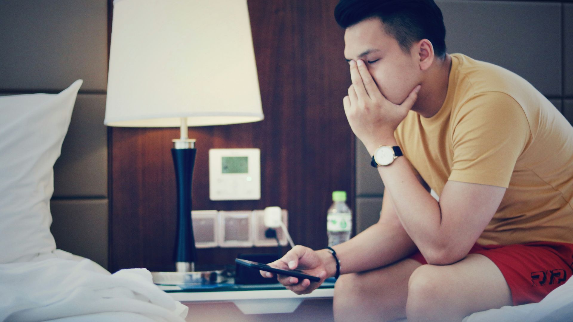 man holding phone and sitting while putting left hand on his face