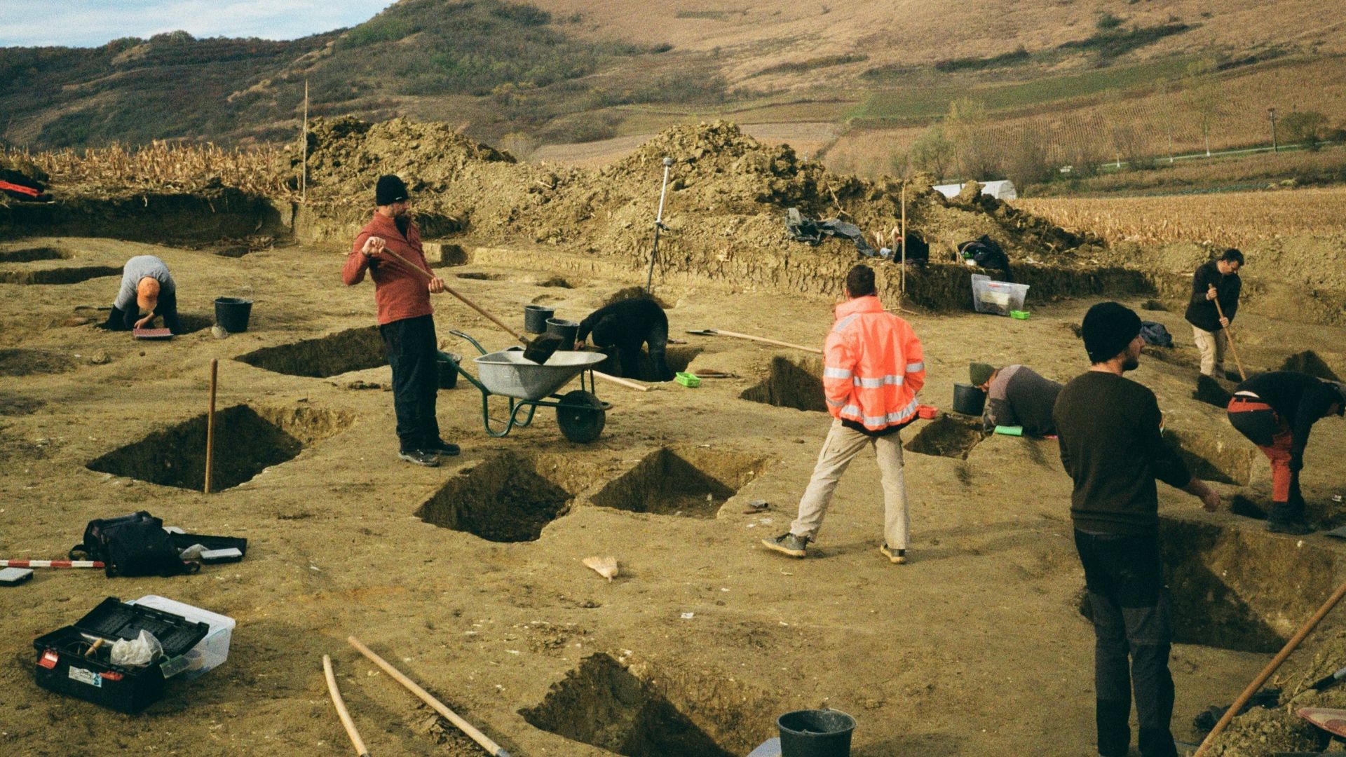 Archaeologists excavating a field with tools and trenches.