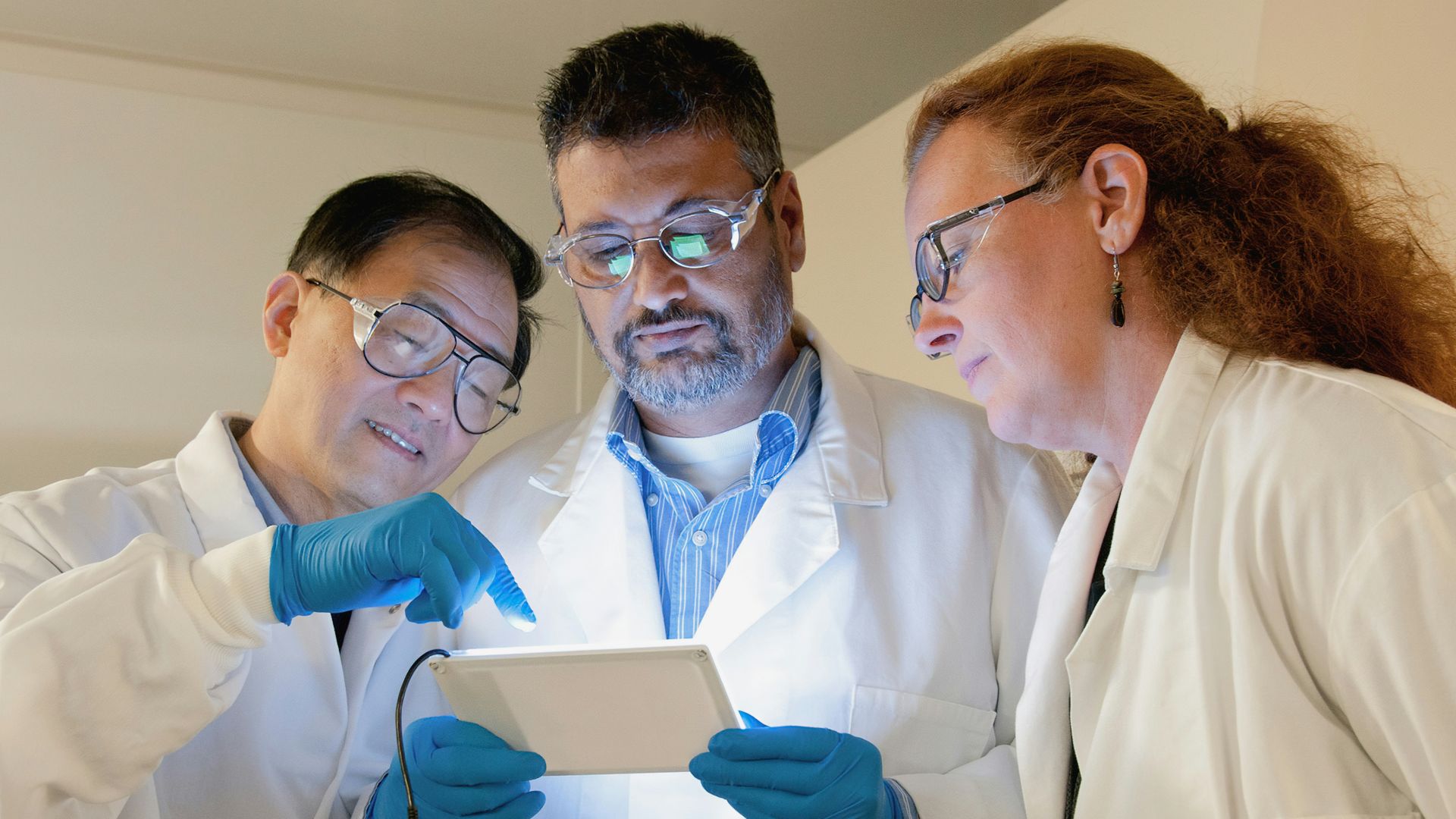 three people in lab coats looking at a tablet