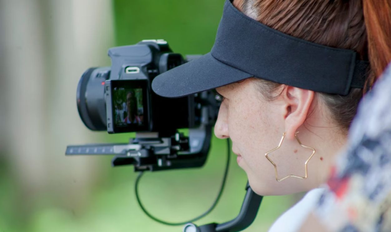 A female camerawoman with star earrings capturing a scene outdoors
