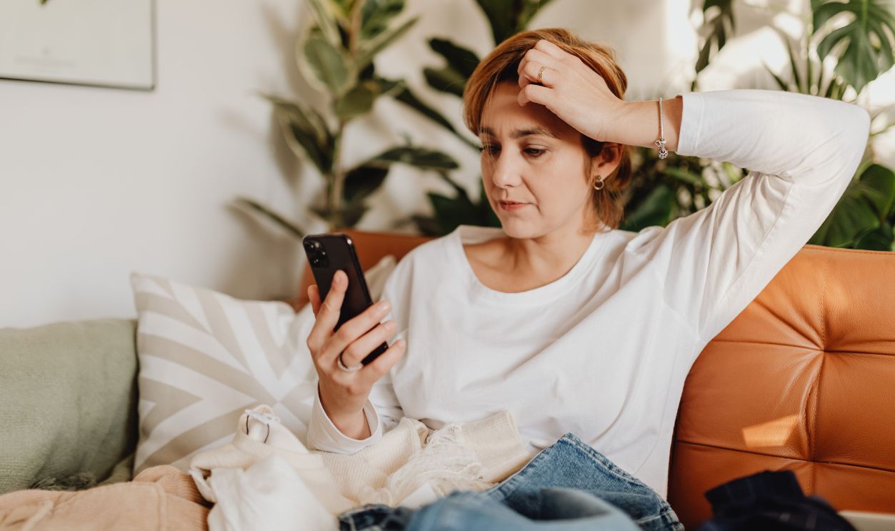 Young woman in white blouse using smartphone while sitting on an orange sofa