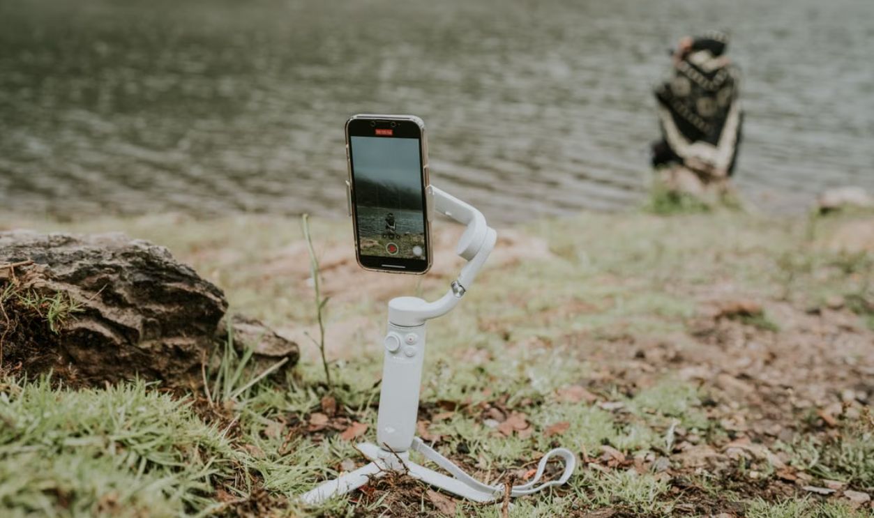 A smartphone on a gimbal capturing a tranquil lakeside scene with a person in the distance