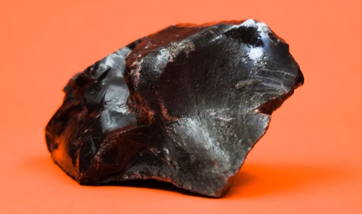 Close-up shot of a glossy obsidian stone with a sharp texture against a vibrant orange background