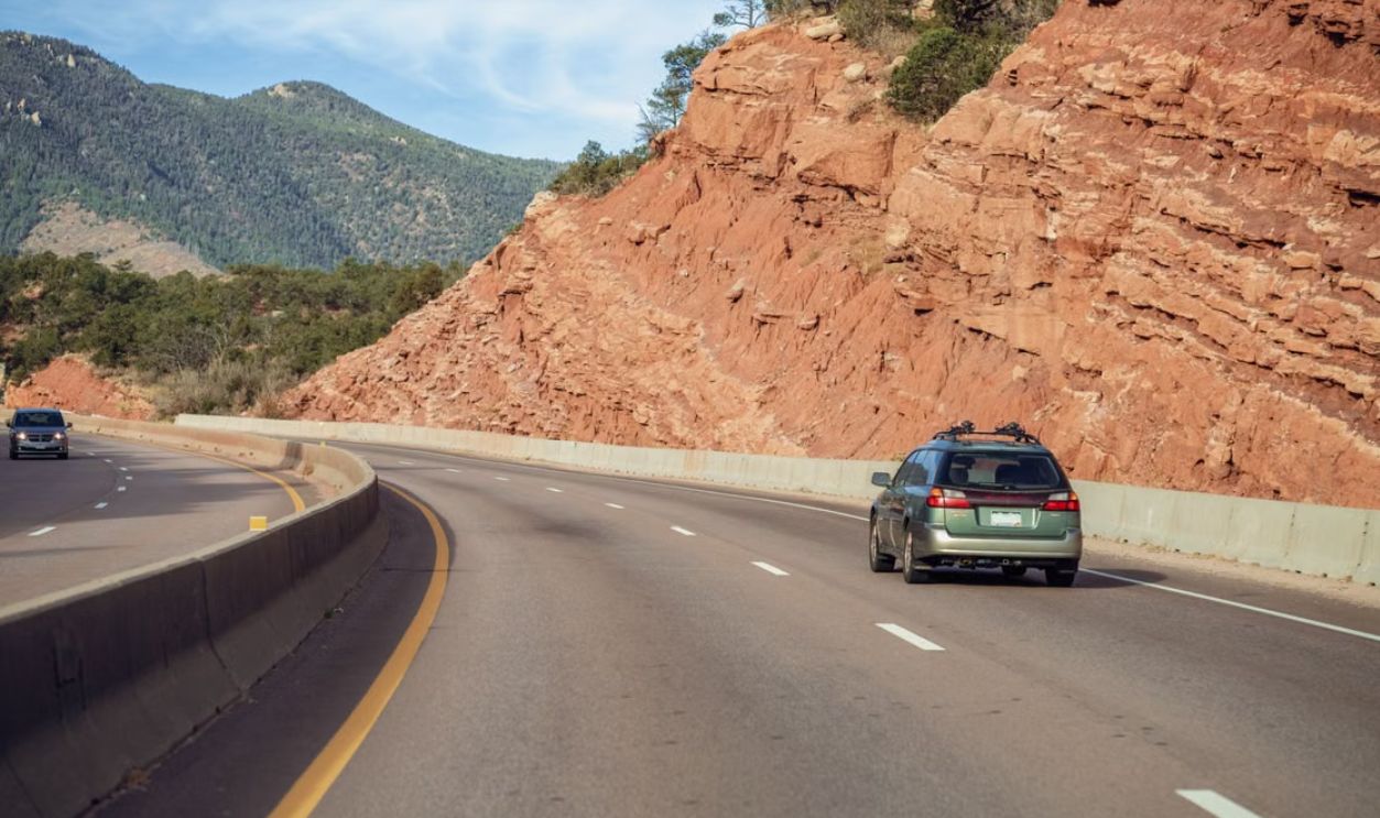 A green car traveling along a Colorado highway surrounded by red rock formations and mountains