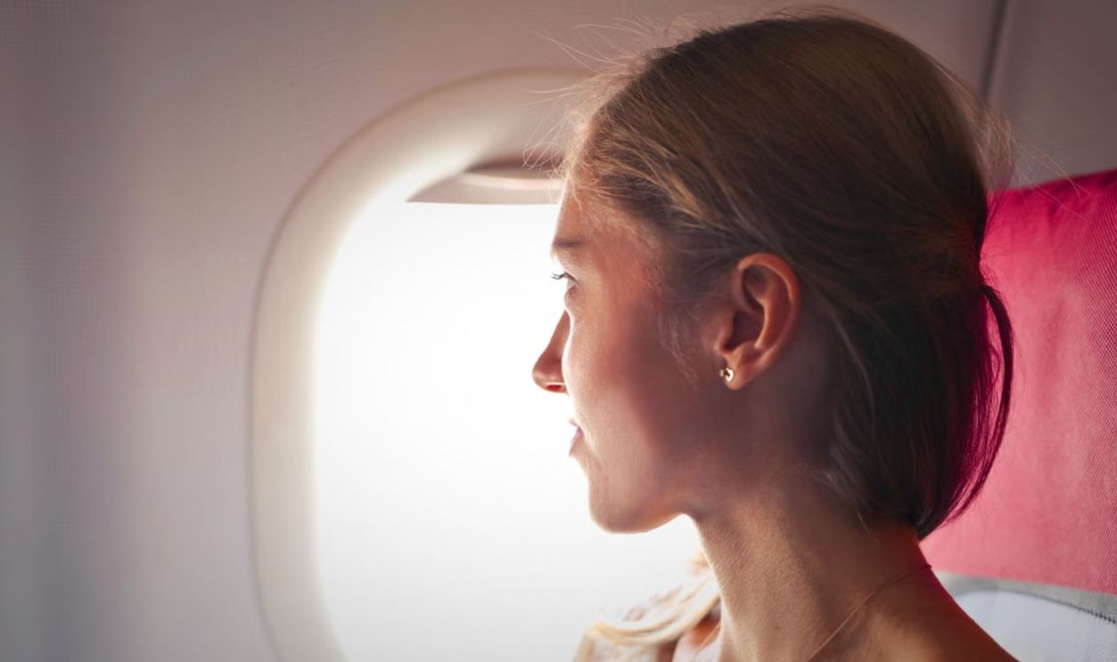 A woman gazes thoughtfully out the window of an airplane during her journey