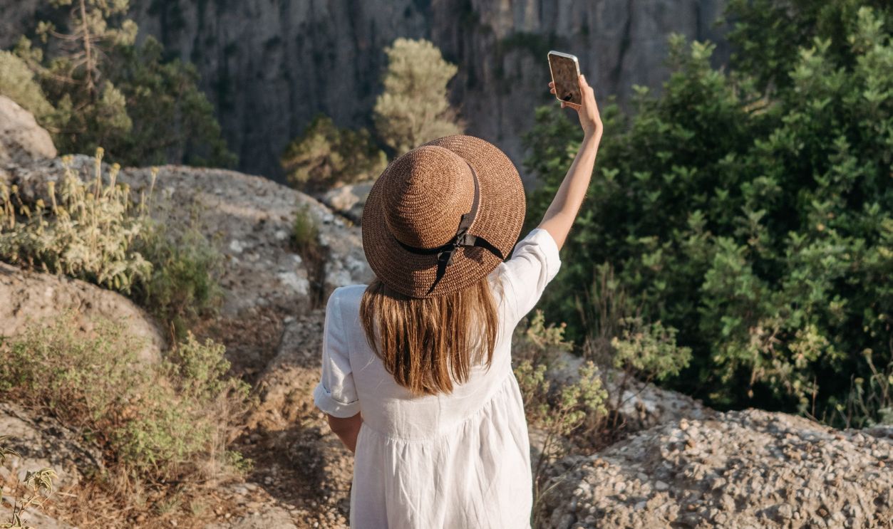 Woman in a hat taking a selfie in a scenic canyon landscape on a sunny day