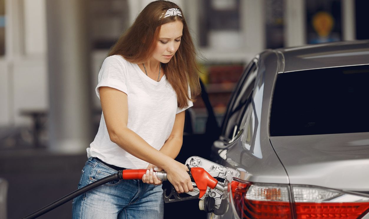 Woman in casual attire refueling a car at a gas station on a sunny day