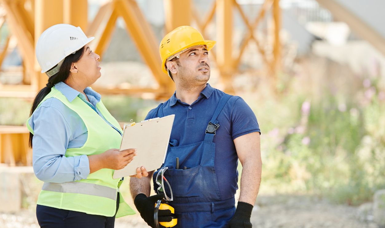 Two construction workers in safety gear discussing site plans at an outdoor construction site