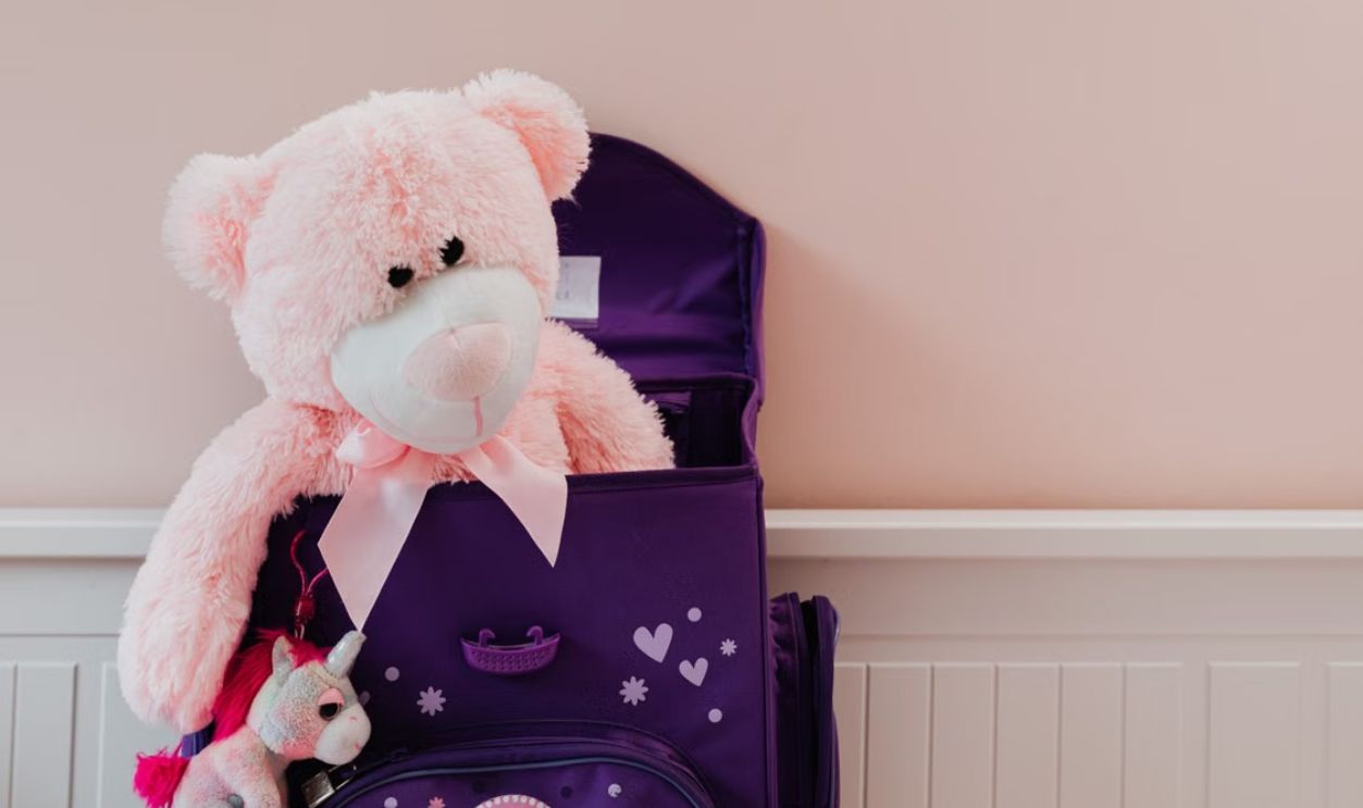 A pink teddy bear and unicorn plush toy in a purple backpack. Perfect for kids' room decor.