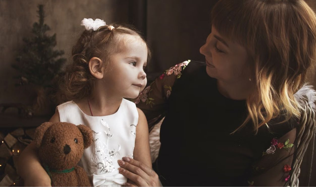 A loving moment between a mother and her daughter with a teddy bear in a cozy indoor setting.