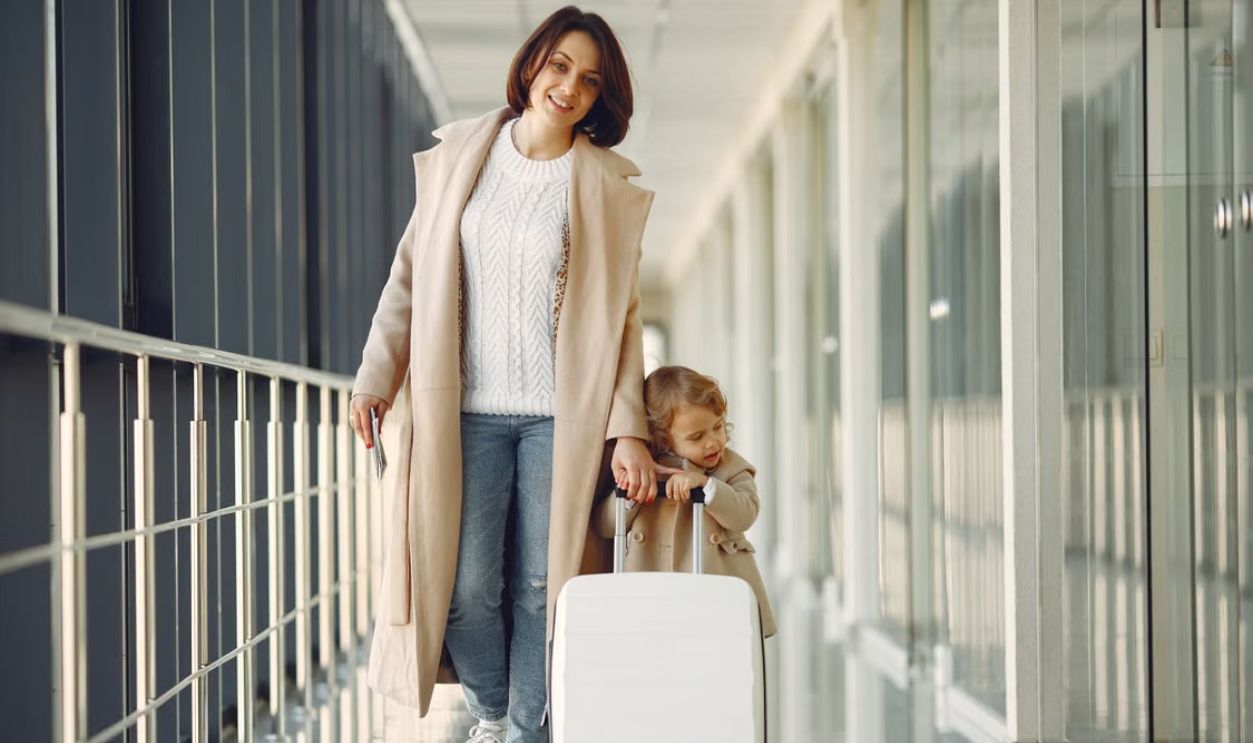 A mother and her daughter walking together in an airport terminal with luggage.