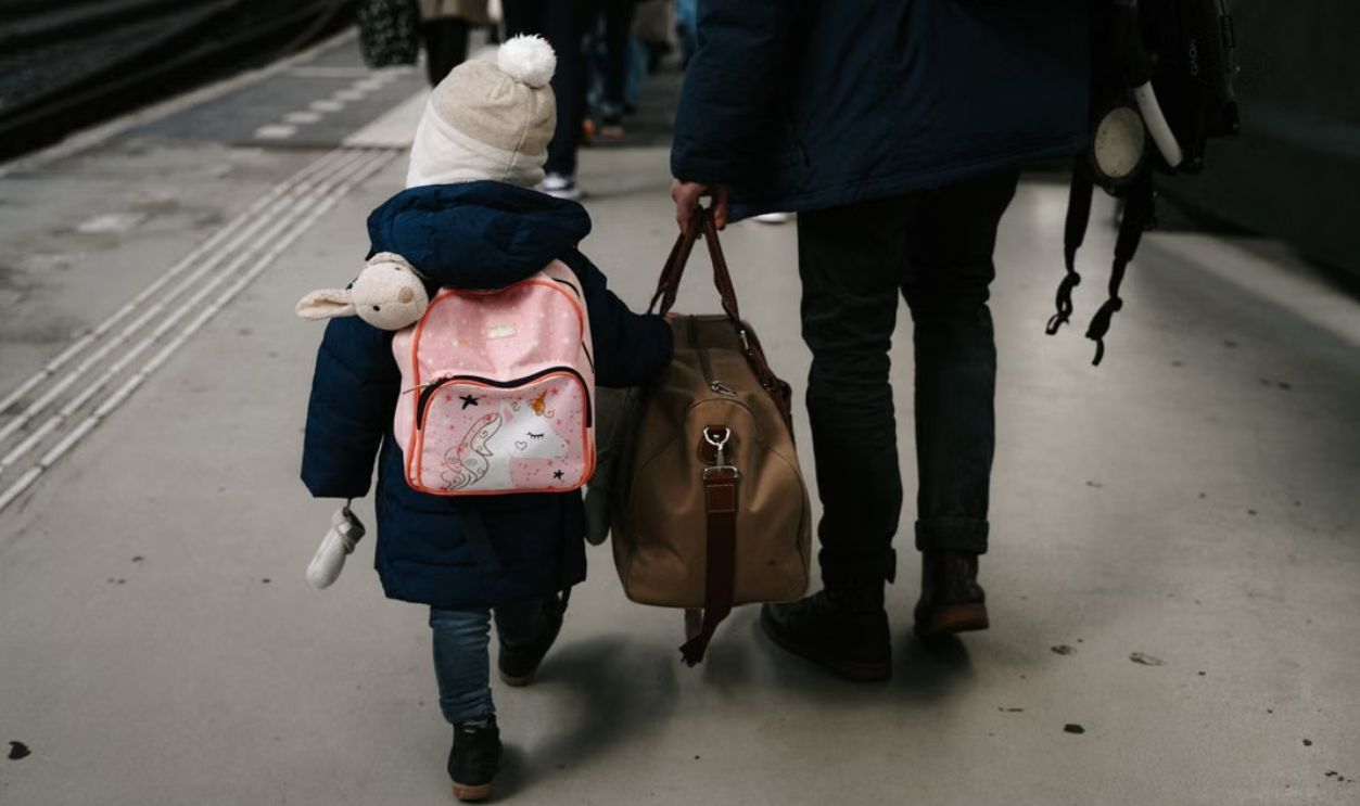 A child and adult carrying bags at a train station platform in Amsterdam.
