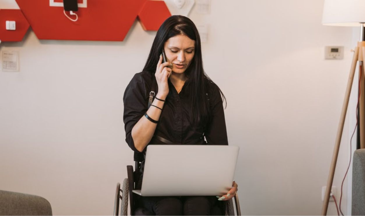 Woman in a wheelchair multitasking with a laptop and phone