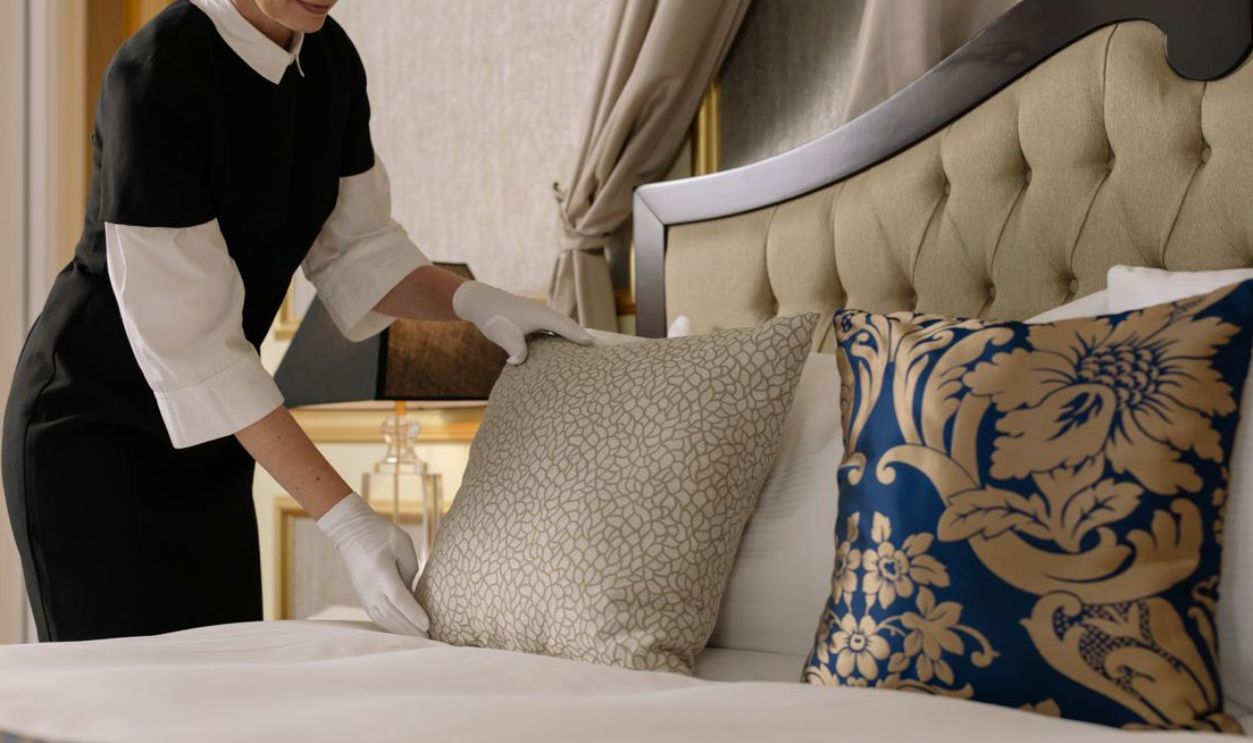 A chambermaid arranges pillows in a luxurious hotel room, showcasing comfort and elegance