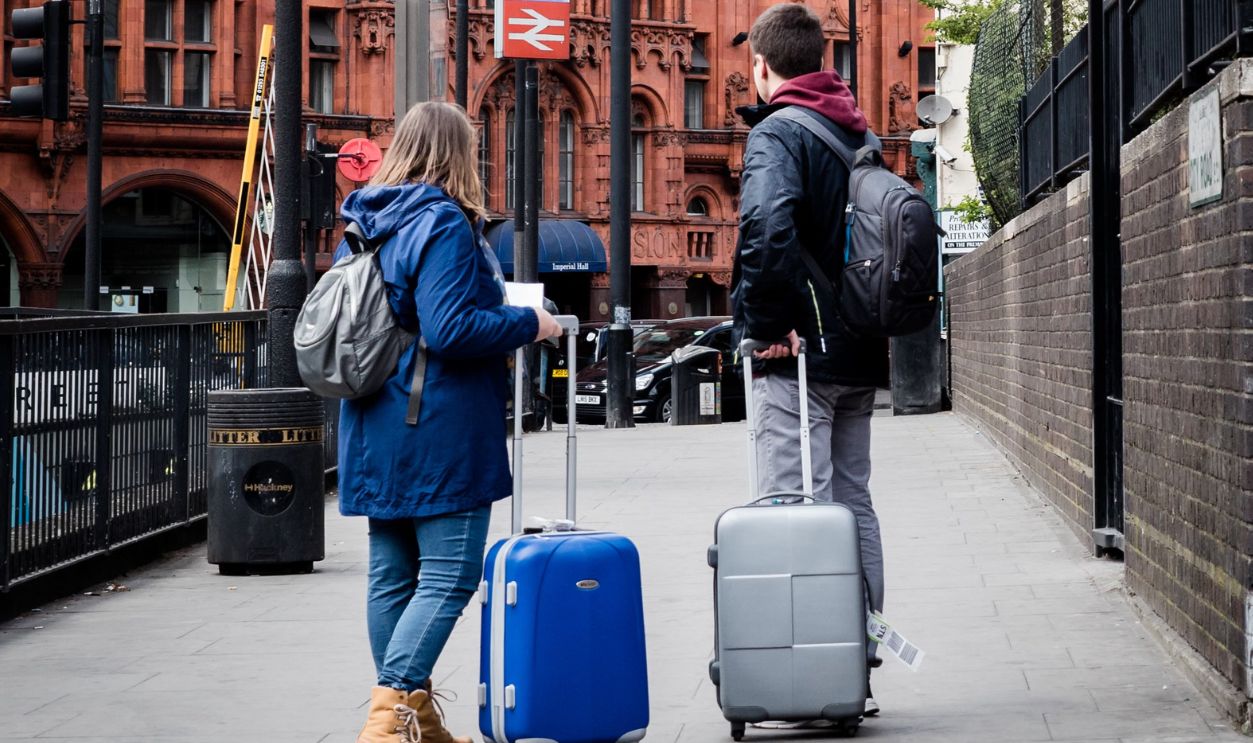A couple with suitcases stands on a London sidewalk, showcasing urban travel and architecture