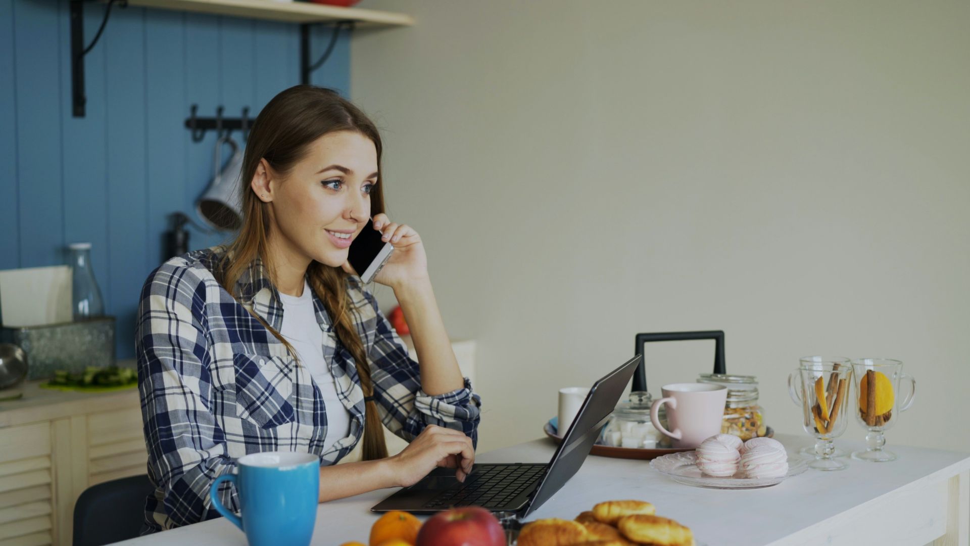 Woman talking on phone while working on laptop at table.