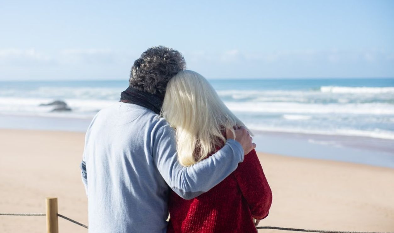 A senior couple embraces by the ocean on a sunny day in Portugal, capturing love and companionship