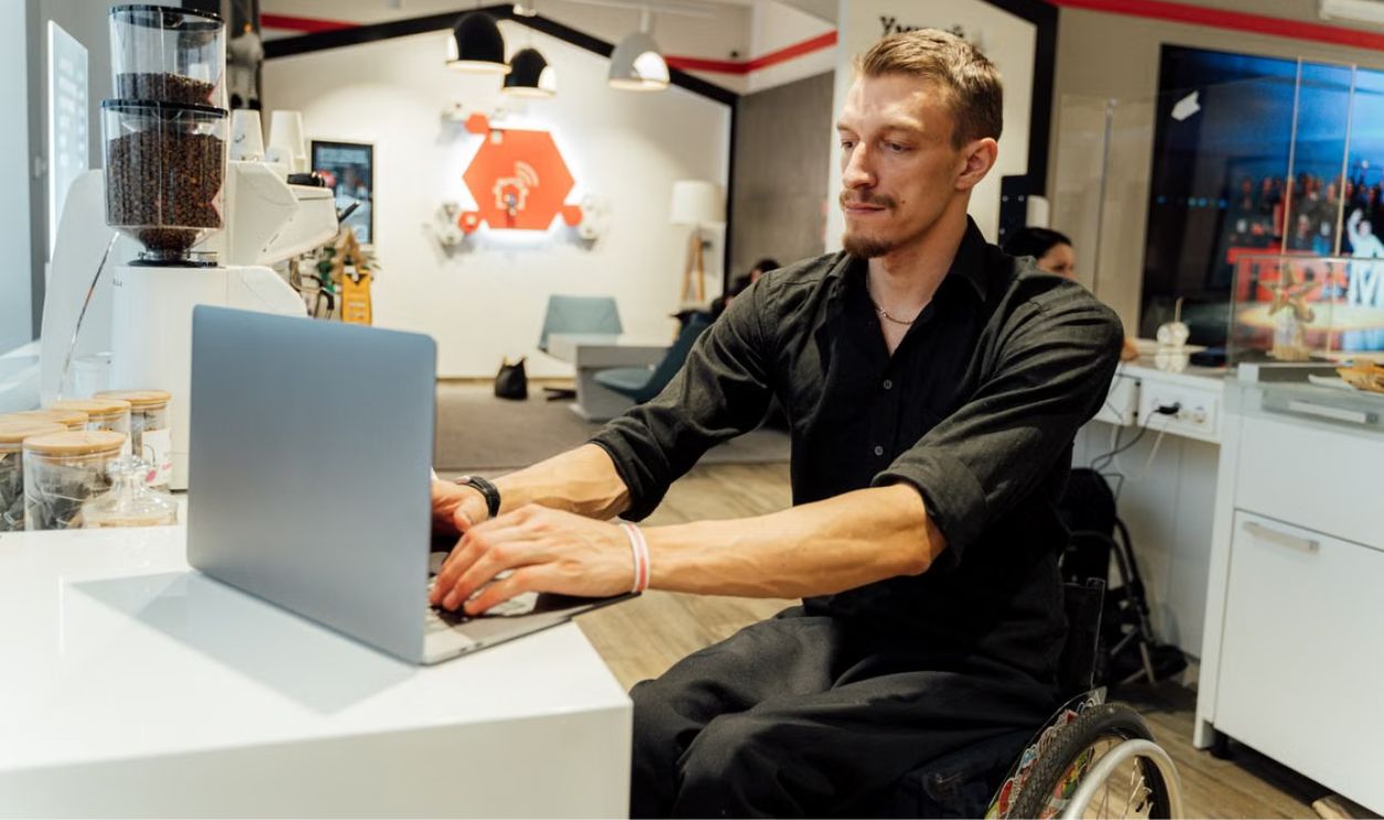 Man in a wheelchair using a laptop in a modern cafe