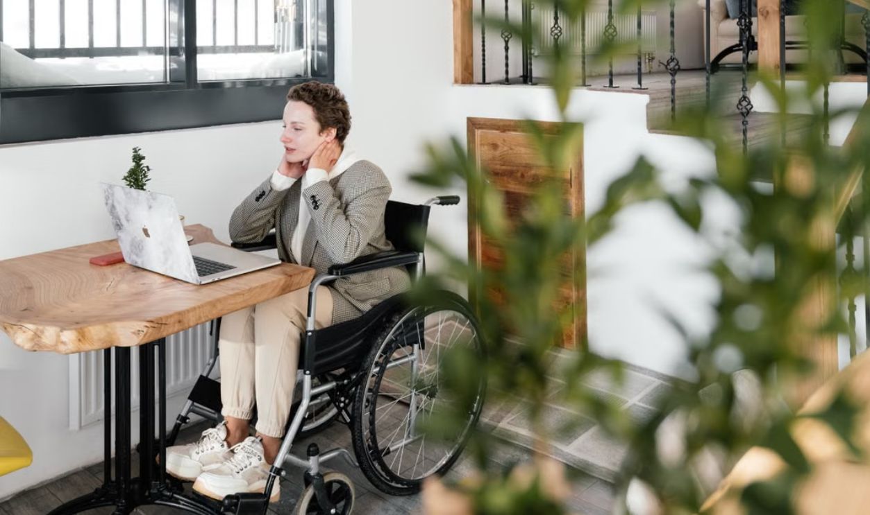 A woman in a wheelchair working on a laptop in a cozy café setting