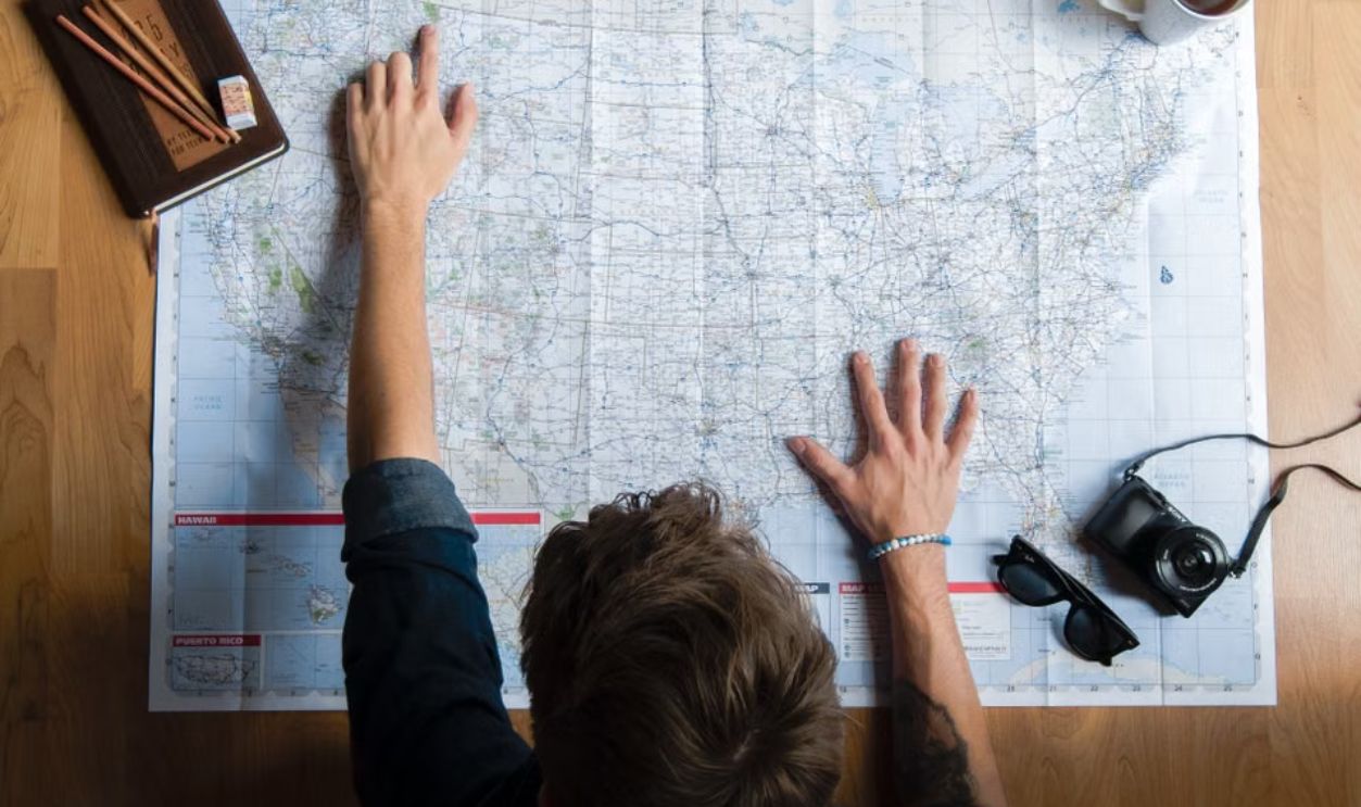 Top view of a man planning a trip with map, camera, and coffee.
