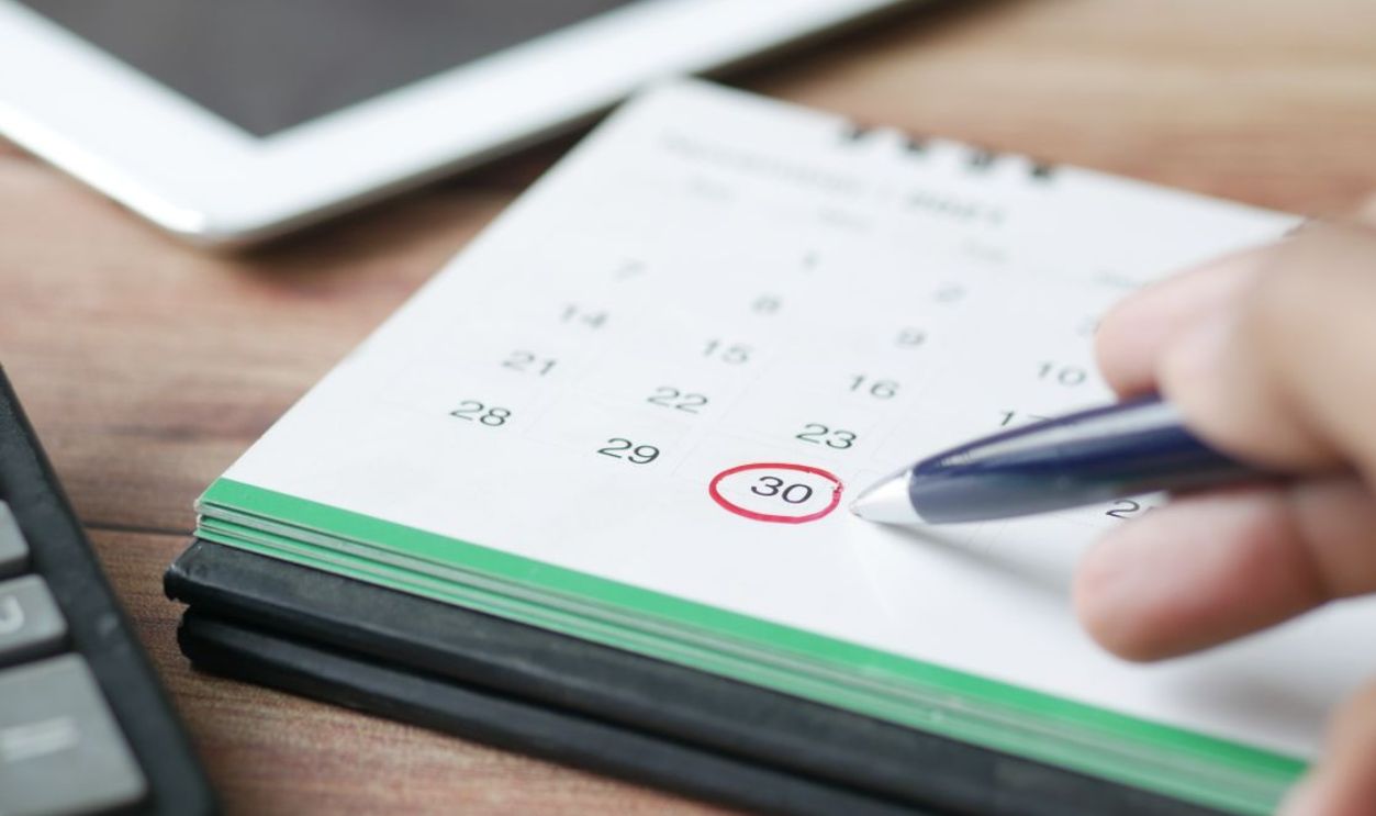 Close-up shot of a hand marking a date on a calendar with a pen, emphasizing planning and scheduling