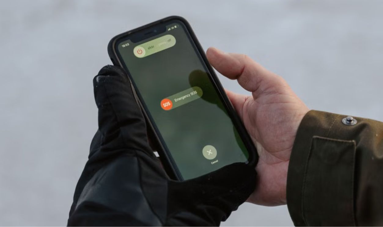Gloved hands holding a smartphone displaying an emergency SOS screen.