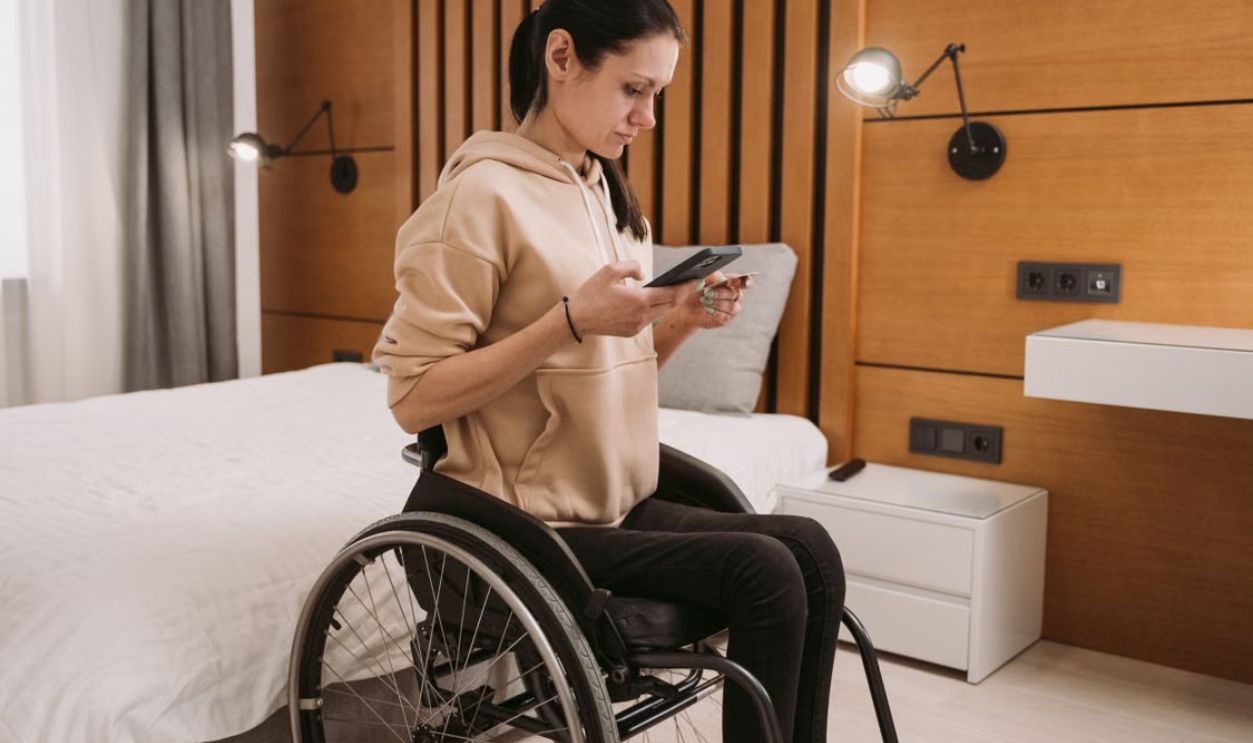 Woman in wheelchair using smartphone in a modern wooden-paneled bedroom