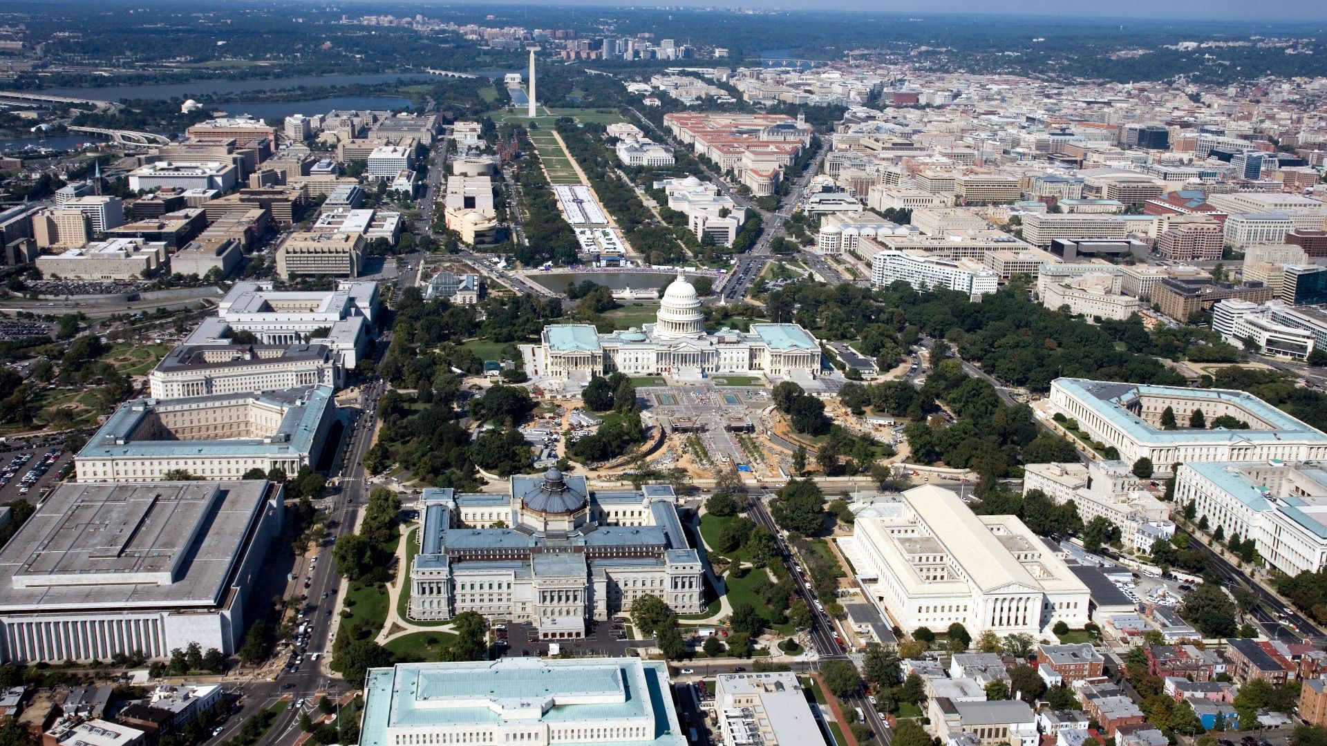 Aerial view (looking west) of Capitol Hill and the National Mall in Washington, D.C. The gov't buildings in the foregrounds:
The white-domed building at the center is the US Capitol.
In front of the Capitol:
(right) with a pale-beige roof and a portico is