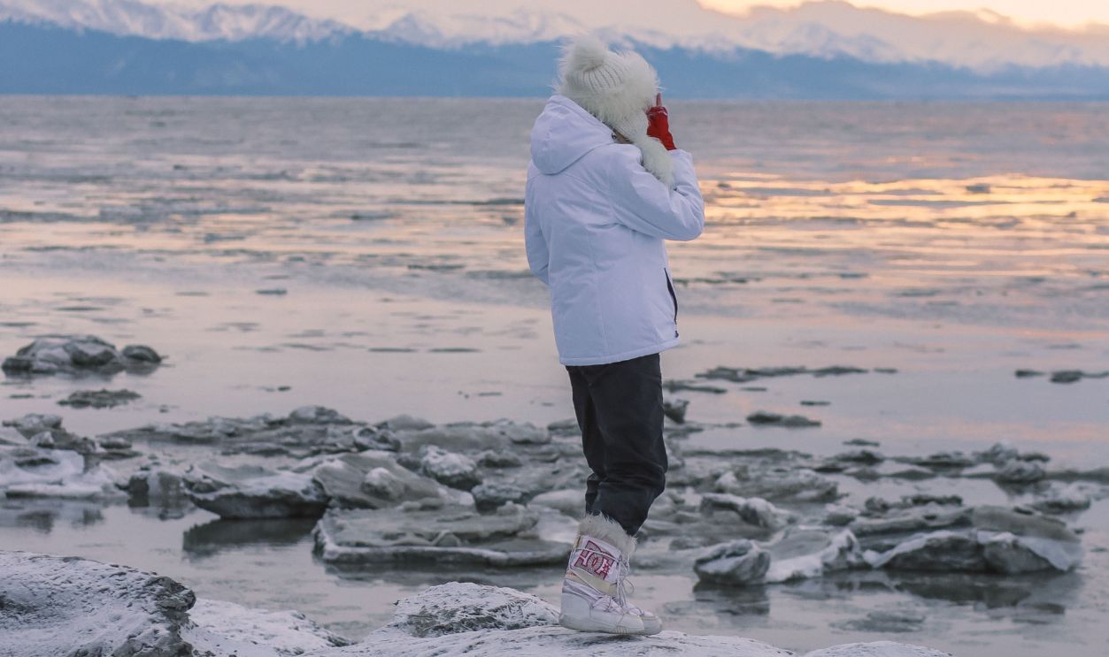 A traveler in winter clothing stands on ice by Anchorage, Alaska,