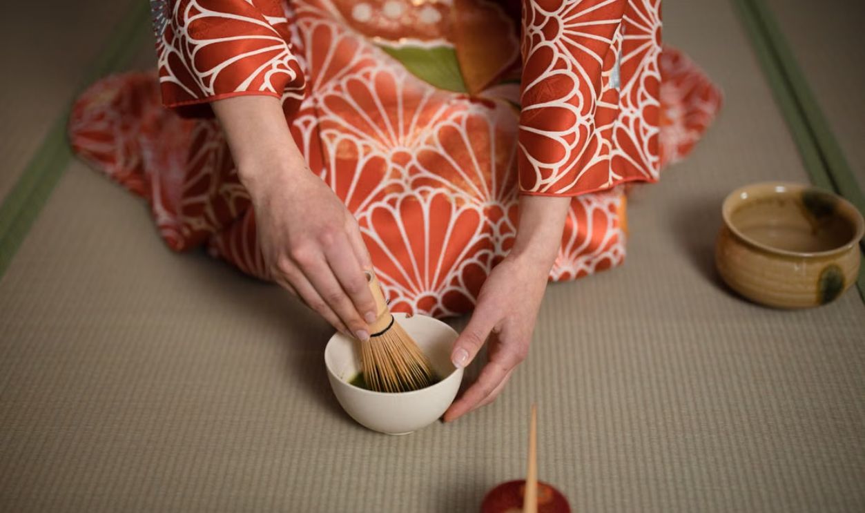 A person in a kimono preparing matcha tea in a traditional ceremony setting.