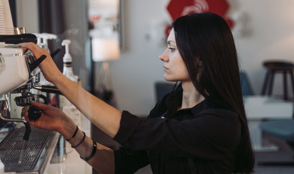A female barista prepares coffee using an espresso machine in a cozy cafe.