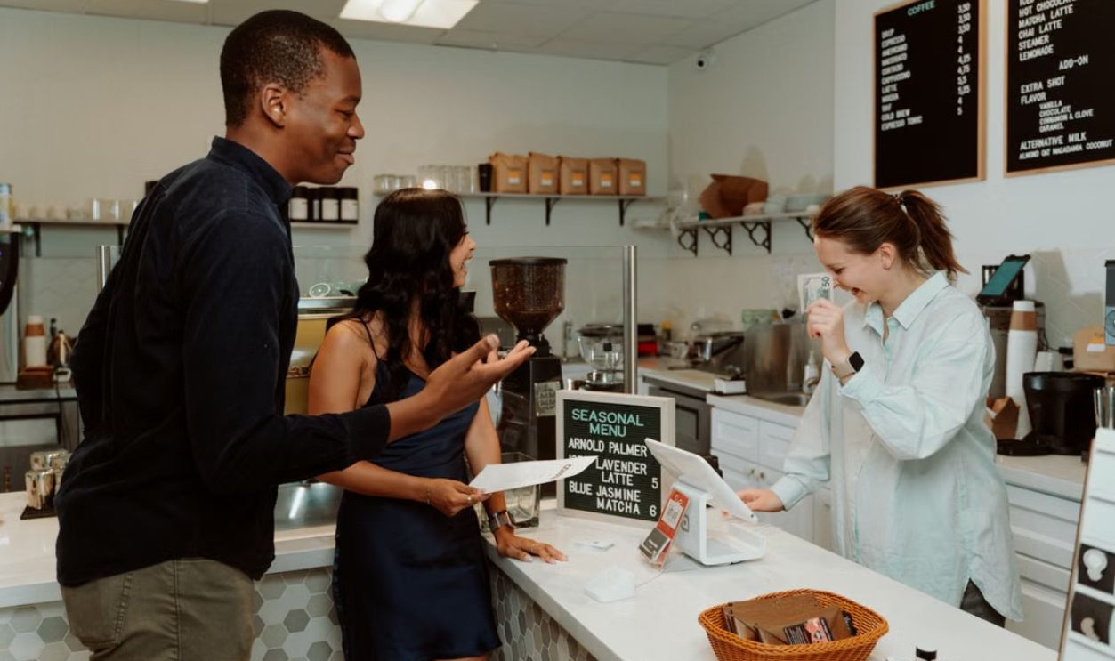Two customers enjoy a lively interaction with a barista at a modern cafe counter, creating a warm and inviting atmosphere.