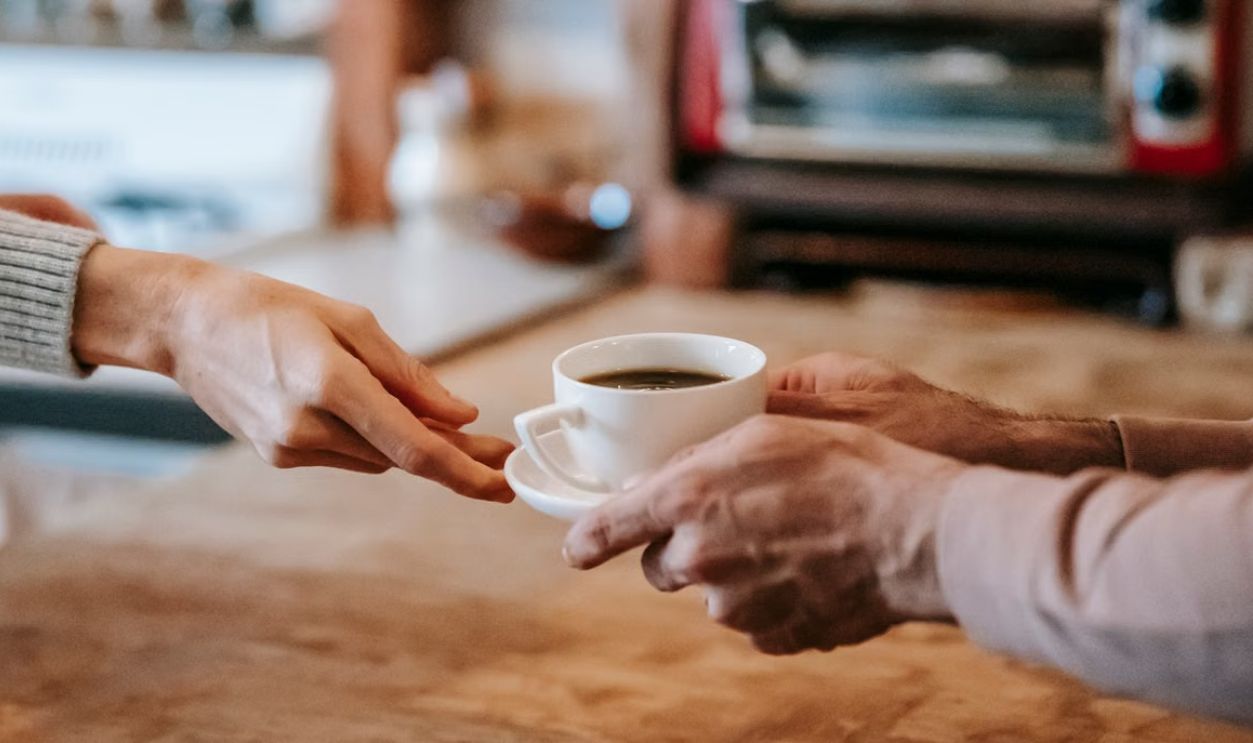 A close-up of two people exchanging a cup of coffee, symbolizing warmth and connection.