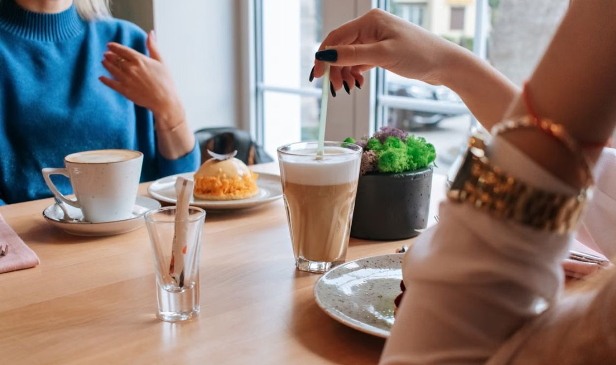 Two women enjoy coffee and dessert in a cozy cafe setting.