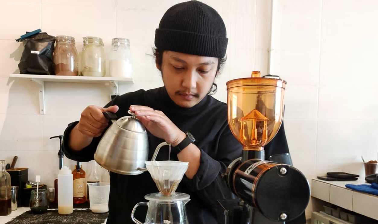A barista expertly brews coffee using the pour over method in a cozy cafe setting in Jakarta.