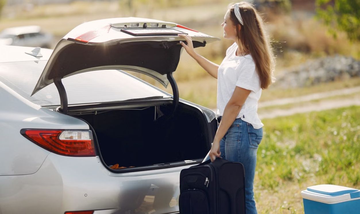 Cheerful woman loading luggage into car trunk, preparing for a summer adventure.